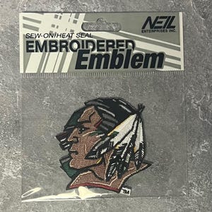 May include: Embroidered emblem featuring a Native American profile with a feathered headdress. The patch is in a clear plastic package with the text "SEW-ON/HEAT SEAL EMBROIDERED Emblem" and the "NEIL ENTERPRISES INC." logo.