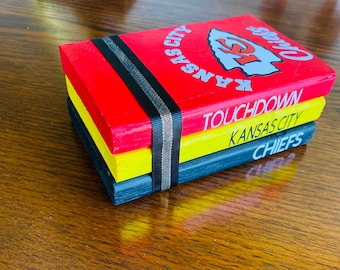 May include: A stack of three wooden blocks with a Kansas City Chiefs theme. The top block is red and features the team's logo and the words "Kansas City Chiefs". The middle block is yellow and says "Touchdown". The bottom block is black and says "Chiefs".