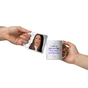 May include: Two white ceramic mugs with butterfly designs and the text "I am a butterfly. Soy una mariposa." One mug features a portrait of a woman. The mugs are held by hands.