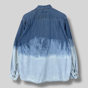 May include: A long-sleeved denim shirt with a unique, faded blue tie-dye effect. The shirt features a classic collar, buttoned cuffs, and a button-down front. The color transitions from a darker blue at the top to a lighter blue at the bottom.