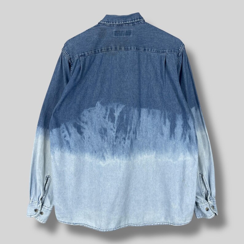 May include: A long-sleeved denim shirt with a unique, faded blue tie-dye effect. The shirt features a classic collar, buttoned cuffs, and a button-down front. The color transitions from a darker blue at the top to a lighter blue at the bottom.