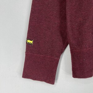 Puede incluir: Una sudadera de manga larga color granate con un dise&ntilde;o de perro bordado en amarillo en la manga izquierda.