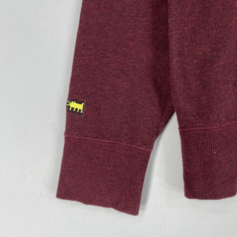 Puede incluir: Una sudadera de manga larga color granate con un dise&ntilde;o de perro bordado en amarillo en la manga izquierda.