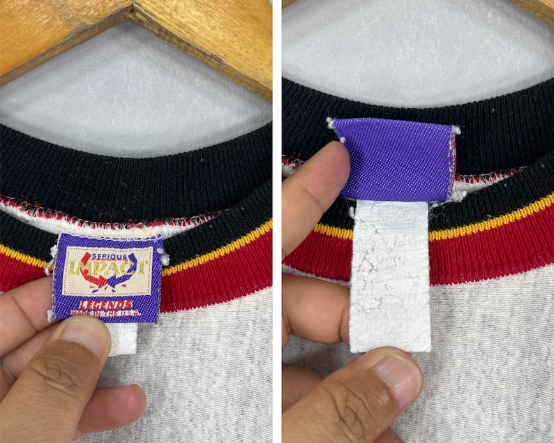 Puede incluir: Primer plano de una sudadera gris de cuello redondo con cuello negro y rayas rojas y amarillas. La etiqueta dice "SERIOUS IMPACT LEGENDS" en un rect&aacute;ngulo azul.