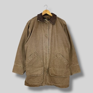Puede incluir: Chaqueta vaquera marrón con cuello de pana. La chaqueta tiene cuatro bolsillos delanteros y cierre de botones. Cuelga de una percha de madera.