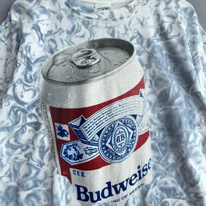 May include: A white t-shirt with a tie-dye pattern featuring a Budweiser beer can with the text "Budweiser King of Beers" and "12 fl. oz."