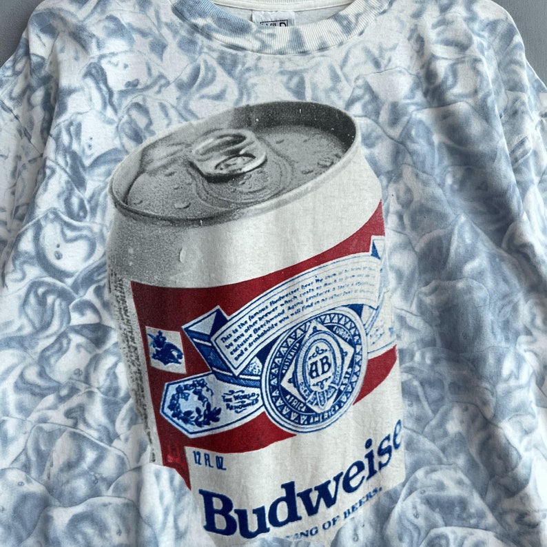 May include: A white t-shirt with a tie-dye pattern featuring a Budweiser beer can with the text "Budweiser King of Beers" and "12 fl. oz."