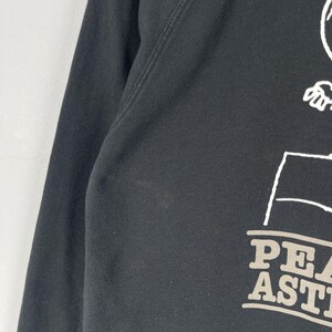 May include: Black sweatshirt with white and gray graphic text that reads "PEA ASTI". The sweatshirt has a crew neck and long sleeves. The graphic appears to be a cartoon character.