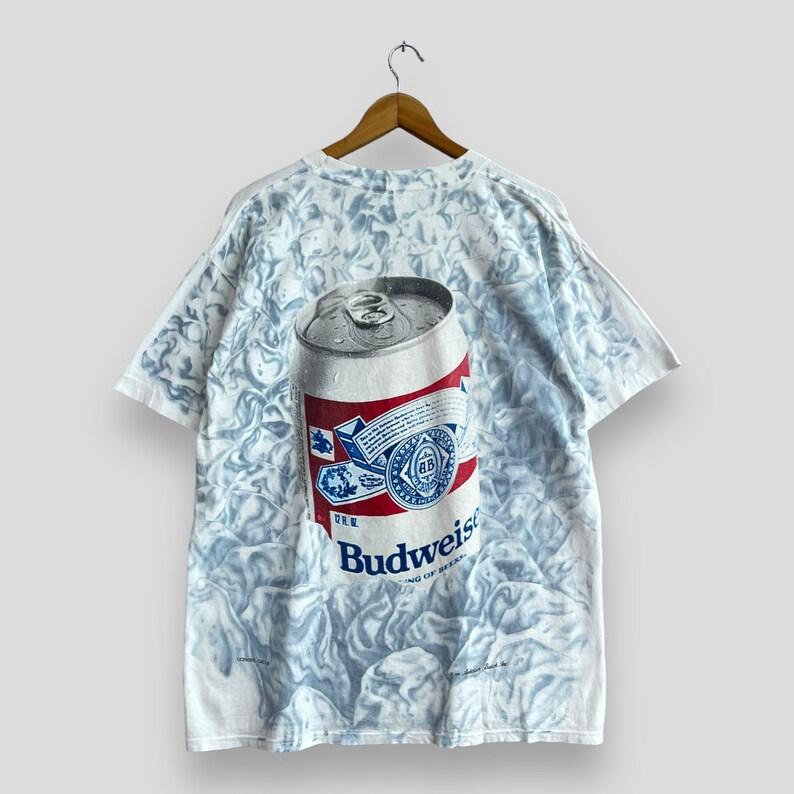 May include: White t-shirt with a tie-dye pattern and a large graphic of a Budweiser beer can. The can is blue, red, and white with the Budweiser logo.