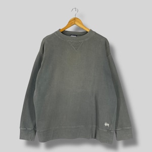 May include: A grey sweatshirt with a small white logo on the bottom right corner. The sweatshirt has a crew neck and long sleeves.