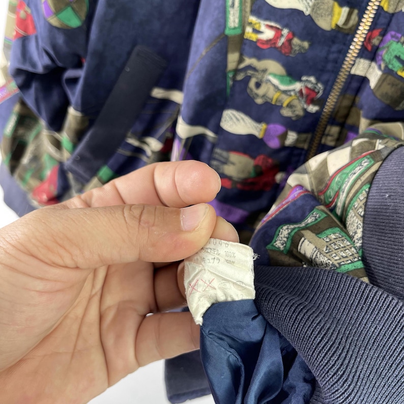 May include: A navy blue bomber jacket with a colorful pattern of horses and riders. The jacket has a zipper closure and a white tag with text that reads "U.S.A. 100% Nylon 377 7448".