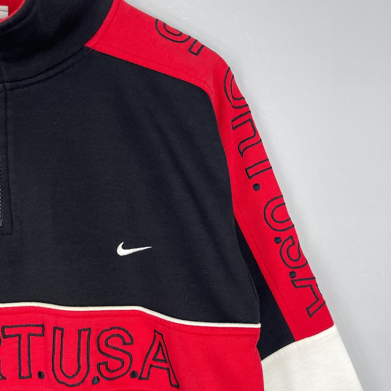 Może przedstawiać: Czarno-czerwona bluza z zamkiem na 1/4 i białym logo Nike swoosh oraz napisem "NI.T.USA" z przodu.