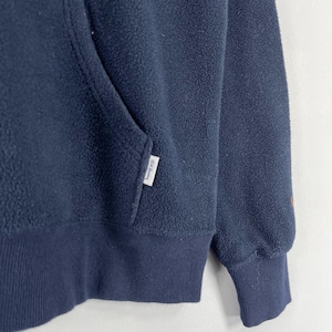 Puede incluir: Primer plano de una sudadera con capucha de forro polar azul marino. La sudadera con capucha tiene un bolsillo de canguro, pu&ntilde;os acanalados y un dobladillo acanalado. Una peque&ntilde;a etiqueta blanca con texto est&aacute; cosida en el bolsillo. El forro polar tiene un aspecto suave y texturizado.