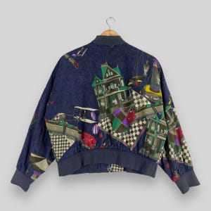 May include: A blue bomber jacket with a colorful print of a house, checkered patterns, and other abstract designs. The jacket has a zipper closure and ribbed cuffs and hem.