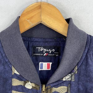 May include: A navy blue bomber jacket with a  "Tomys" label and a French flag patch. The jacket has a zipper closure and a printed pattern of various objects.