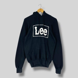 May include: A black hoodie featuring the white "Lee" logo within a white rectangle on the front. It has a kangaroo pocket and a drawstring hood. The long sleeves have ribbed cuffs.