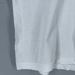 Puede incluir: Camiseta blanca con un ligero pliegue en la tela. La camiseta tiene algunos peque&ntilde;os agujeros.