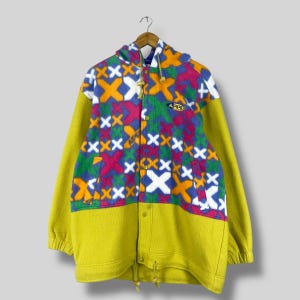 May include: A yellow, green, blue, pink, and orange fleece jacket with a colorful geometric pattern and a hood. The jacket has a zipper closure and a button placket. The jacket has a logo that says "APPL" on the front.