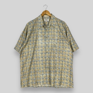 Könnte beinhalten: Ein kurzärmeliges, blau-goldenes Hemd mit Knöpfen und geometrischem Muster. Das Hemd hat einen Kragen und eine Tasche auf der linken Seite.