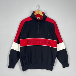 Może przedstawiać: Czarna i czerwona vintage bluza Nike z zamkiem błyskawicznym na p&oacute;ł i napisem "SPORT.USA" z przodu. Bluza ma białe akcenty na rękawach.