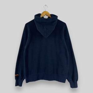 Puede incluir: Sudadera con capucha azul marino con capucha con cord&oacute;n y mangas largas. La sudadera con capucha cuelga de una percha de madera. La manga tiene un dise&ntilde;o bordado en naranja. La sudadera con capucha est&aacute; hecha de un material suave y c&oacute;modo.