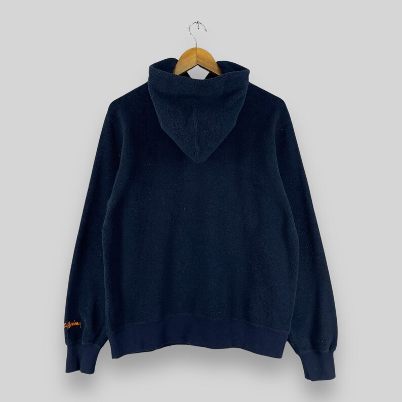 Puede incluir: Sudadera con capucha azul marino con capucha con cord&oacute;n y mangas largas. La sudadera con capucha cuelga de una percha de madera. La manga tiene un dise&ntilde;o bordado en naranja. La sudadera con capucha est&aacute; hecha de un material suave y c&oacute;modo.