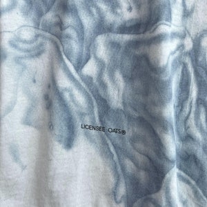 May include: Close-up of a white fabric with a blue tie-dye pattern. The fabric has the text "LICENSEE OATS&reg;" printed on it.