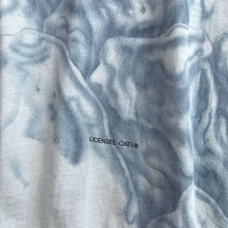 May include: Close-up of a white fabric with a blue tie-dye pattern. The fabric has the text "LICENSEE OATS&reg;" printed on it.