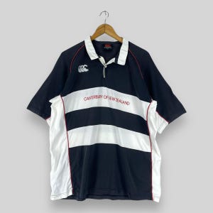 May include: Black and white striped rugby shirt with red trim. The shirt has the Canterbury of New Zealand logo and text on the front.