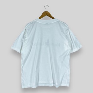 Puede incluir: Camiseta blanca de manga corta con un peque&ntilde;o logotipo descolorido en la parte delantera.