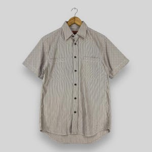 May include: A striped short-sleeved button-down shirt with two chest pockets. The shirt is light brown with white stripes.