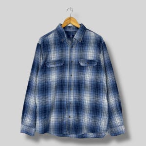 May include: A blue and white checked flannel shirt with two chest pockets and button fastenings. The long-sleeved shirt is hanging on a wooden hanger.