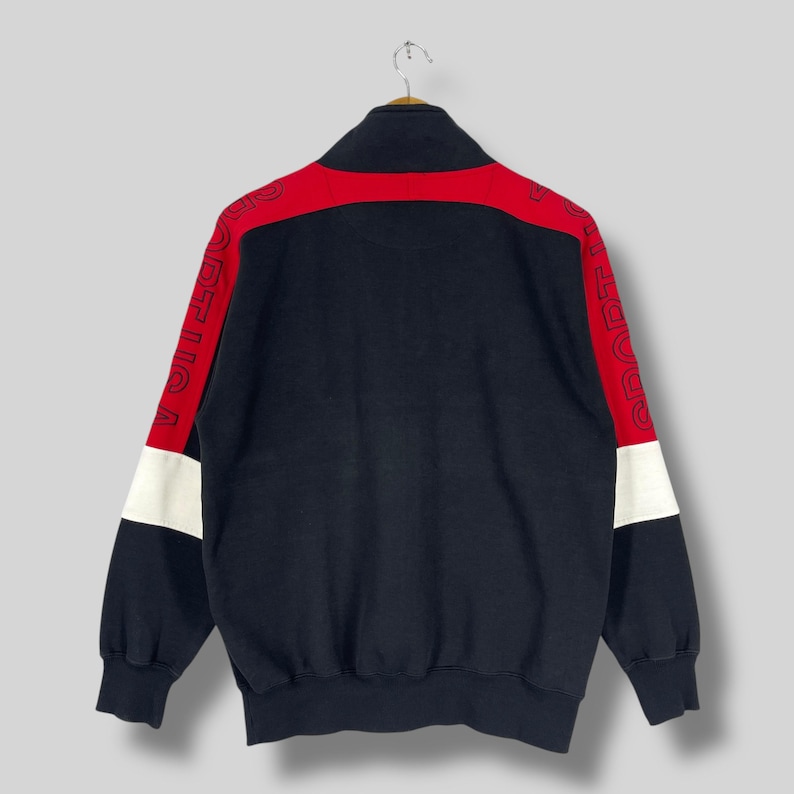 Może przedstawiać: Czarna bluza zapinana na zamek błyskawiczny z czerwonymi i białymi paskami na rękawach. Rękawy mają nadrukowany tekst "SPORTICA" w białym obramowaniu.