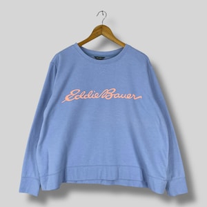 May include: A light blue sweatshirt with long sleeves and a crew neck, hanging on a wooden hanger. The sweatshirt features the text "Eddie Bauer" in a coral-colored script across the chest.