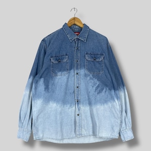 May include: A long-sleeved denim shirt with a gradient effect, transitioning from a darker blue at the shoulders to a lighter blue at the hem. Features two chest pockets and a button-down front. The shirt is hanging on a wooden hanger.