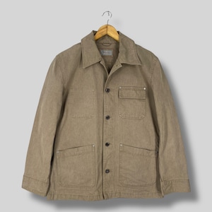May include: A tan corduroy jacket with a collared neckline, four front pockets, and button closures. The jacket is hanging on a wooden hanger against a neutral background. The jacket has a classic, utilitarian design.
