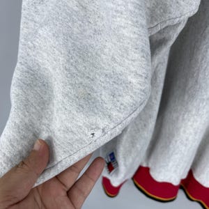 Puede incluir: Primer plano de una sudadera gris con ribete rojo y amarillo. La sudadera tiene un peque&ntilde;o desgarro cerca de la manga. Se ve una peque&ntilde;a etiqueta con colores rojo, blanco y azul.