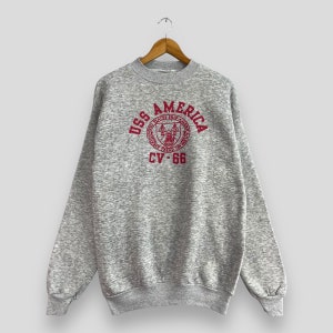 Könnte beinhalten: Grauer Sweatshirt mit einem roten gestickten Logo, auf dem "USS AMERICA" und "CV-66" steht.