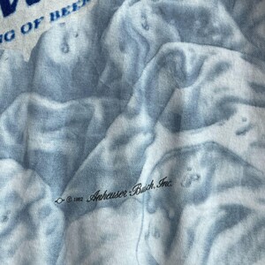 May include: A close-up of a blue and white tie-dye t-shirt with the text "&copy; 1992 Anheuser-Busch, Inc." printed on the fabric.