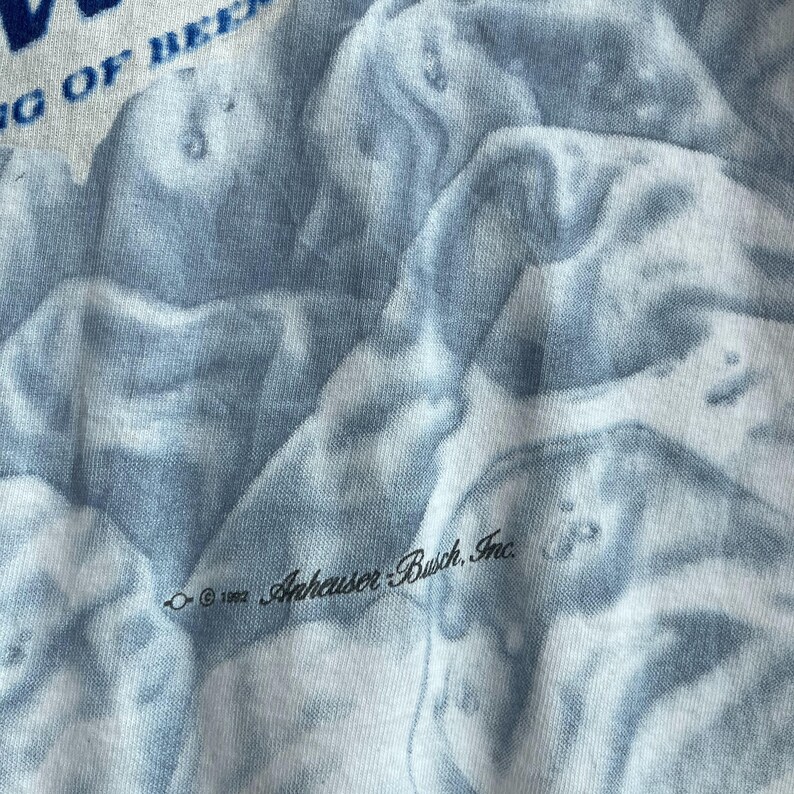 May include: A close-up of a blue and white tie-dye t-shirt with the text "&copy; 1992 Anheuser-Busch, Inc." printed on the fabric.