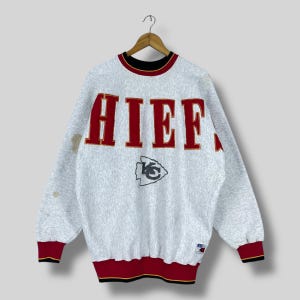 Puede incluir: Una sudadera gris vintage con la palabra "CHIEFS" en letras rojas en el pecho. La sudadera tiene cuello y pu&ntilde;os negros y rojos, y un logotipo del equipo debajo de la palabra.