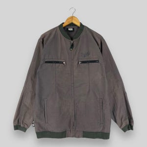Pode incluir: Uma jaqueta bomber cinza com zíper com um logotipo Vans preto no peito esquerdo. A jaqueta tem dois bolsos com zíper na frente e gola e punhos canelados.