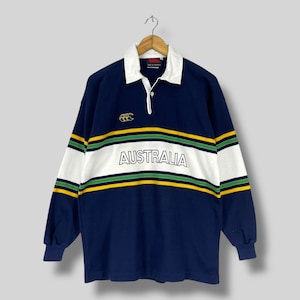 May include: Navy blue long-sleeve rugby shirt with a white collar and the word "AUSTRALIA" across the chest. The shirt features green and yellow stripes and a logo on the left chest.