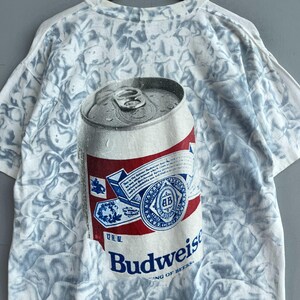 May include: White t-shirt with a tie-dye pattern featuring a Budweiser beer can with the text "Budweiser King of Beers" and "12 FL OZ".