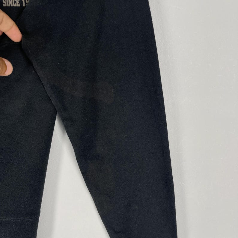 May include: Close-up of a black long-sleeved garment. The fabric appears to be a soft material. Faint text is visible in the upper left corner. The garment is against a white background.