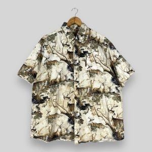 Puede incluir: Una camisa de manga corta con botones, fondo blanco y un patrón de ciervos marrones en un entorno boscoso.