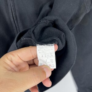May include: Black zip-up sweatshirt with a tag visible. The tag has Japanese text and care symbols. The sweatshirt appears to be made of a soft material. The garment is a size L.
