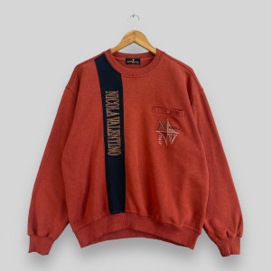 Puede incluir: Sudadera de color óxido con una franja vertical azul marino en la parte delantera, con "NICOLA VALENTINO" en letras doradas. Un pequeño bolsillo con un botón está en el pecho derecho, con un diseño de brújula bordado y el texto "NICOLA ITALY".