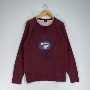 Puede incluir: Una sudadera color burdeos con un gr&aacute;fico azul y blanco de un perro y el texto "American Art 1985 Keith Haring" en la parte delantera.