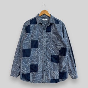 Puede incluir: Una camisa azul de manga larga con botones y diseño de patchwork. La camisa está hecha de una mezcla de algodón y presenta una variedad de patrones azules y blancos.